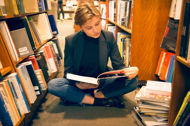 Student girl sitting on the floor and reading a book in the library - Foto, Imagem