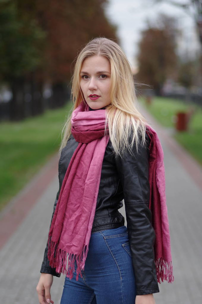 Thoughtful beautiful young woman in leather jacket, blue jeans and red scarf - Fotografie, Obrázek