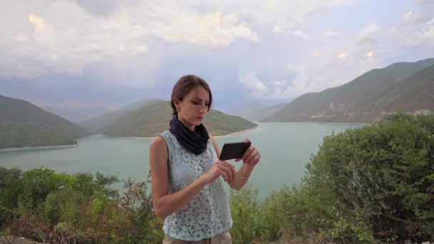湖の近くのスマート フォンを使って若い女性. - 映像、動画