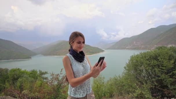 Een jonge dame met behulp van een Smartphone in de buurt van het meer. - Video