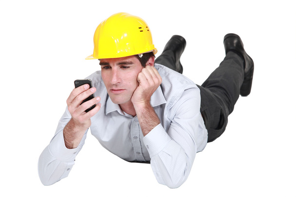 Architect lying on floor looking annoyed at sms - Foto, afbeelding
