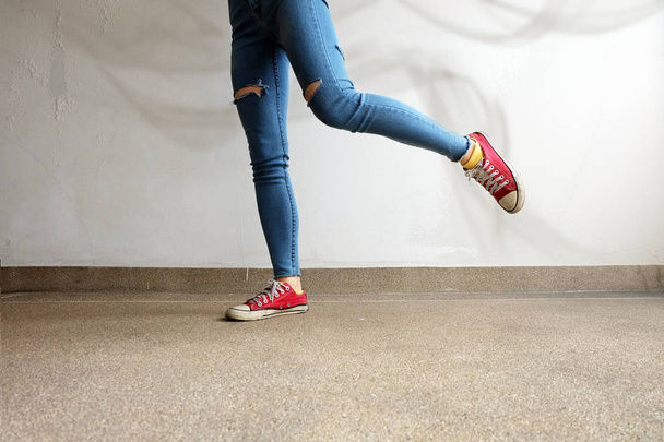 Red Sneakers. Womans Legs in Red Sneakers and Blue Jeans with White Smoke on Floor Background - Foto, immagini