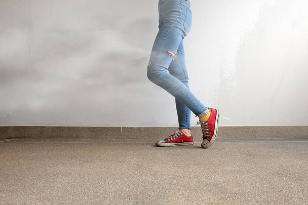 Red Sneakers. Womans Legs in Red Sneakers and Blue Jeans with White Smoke on Floor Background - Фото, изображение