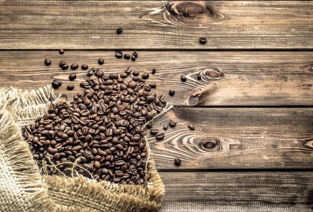 Black coffee beans in burlap sack on wooden table, selective focus - Фото, зображення