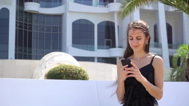 Een jonge dame met behulp van een Smartphone in de buurt van het Hotel. - Video