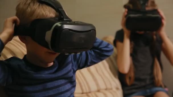 Brother with sister at home sitting on the couch playing the game using virtual reality glasses. Happy family - Materiał filmowy, wideo