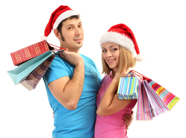 Young couple in Santa hats shopping and holding many shopping bags isolated on white - Foto, Imagem