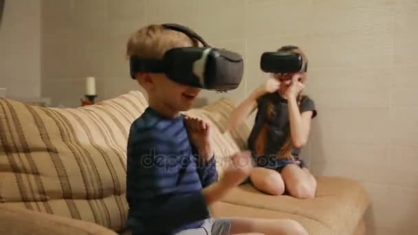 Brother with sister at home sitting on the couch playing the game using virtual reality glasses. Happy family - Filmati, video