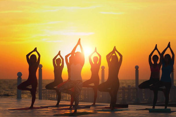 Egy csoportja a nők jóga napkeltekor, a tenger közelében - Fotó, kép
