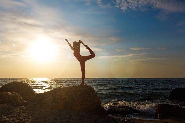 A woman in a red suit practicing yoga on stone at sunrise near the sea - Foto, Imagem