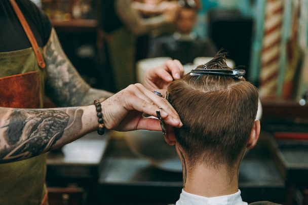 Primer plano de hombre consiguiendo corte de pelo de moda en la peluquería. Peluquero masculino en tatuajes sirviendo al cliente
. - Foto, Imagen