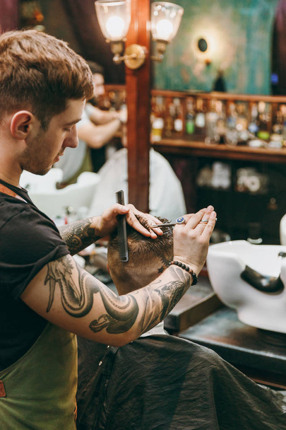 Мужчина стрижется в парикмахерской. Мужчина-парикмахер в татуировках обслуживающий клиента
. - Фото, изображение
