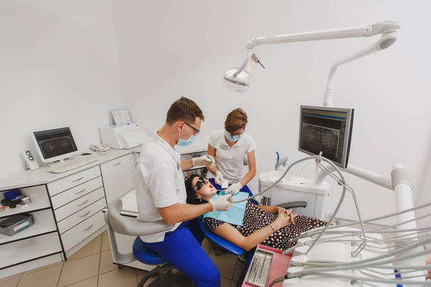 Miespuolinen hammaslääkäri, jolla on naispuolinen avustaja, auttaa hoitamaan naispotilaan hampaita toimistossa sijaitsevassa klinikassa.
 - Valokuva, kuva