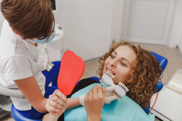 Dentista que compara el tono de los dientes del paciente con muestras para el tratamiento de blanqueamiento
 - Foto, imagen