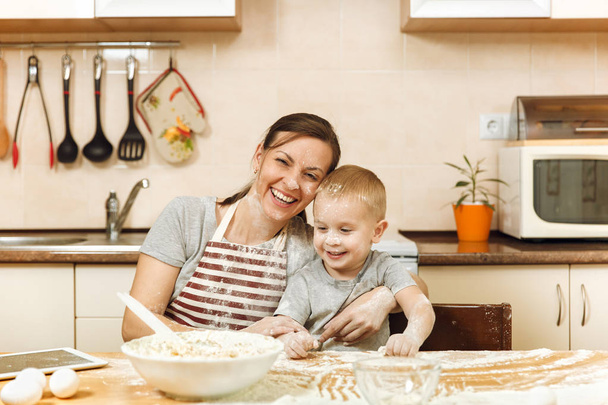 Kleiner Junge hilft Mutter, in heller Küche mit Tablette auf dem Tisch Ingwerkekse zu kochen. glückliche Familienmutter 30-35 Jahre und Kind 2-3 am Wochenendmorgen zu Hause. Beziehungskonzept - Foto, Bild