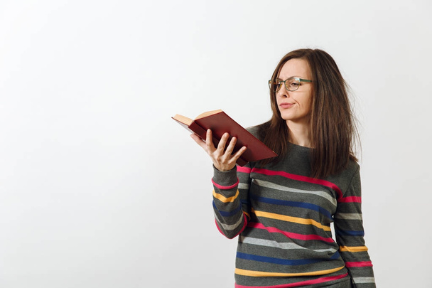 Beautiful European young brown-haired woman in glasses for sight dressed in casual dark grey longsleeve with colorful stripes, standing with book on a white background. Reading and studying concept. - Foto, Bild
