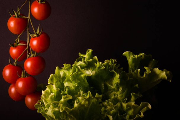 Bunch of fresh cherry tomatoes and green salad on a black backgr - Foto, Imagem