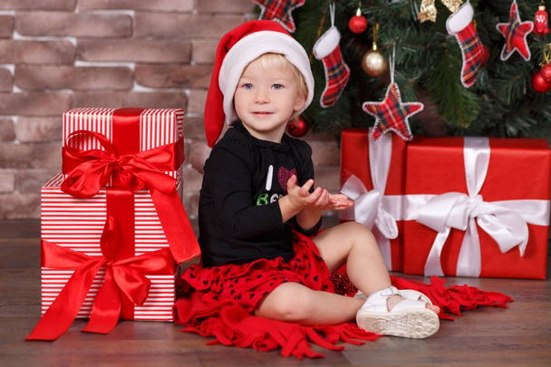 Christmas beautiful cute baby girl posing in casual clothes close to new year pine green tree with presents pillows and toy horse in studio scene - Фото, зображення