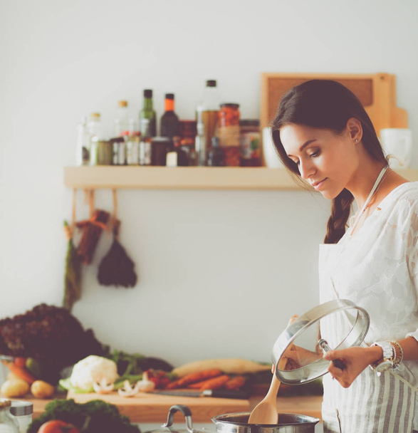 Young woman standing by the stove in the kitchen - Foto, imagen