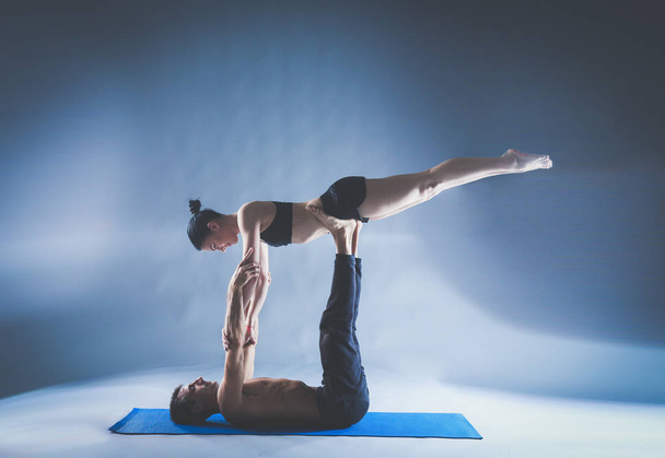 Young couple practicing acro yoga on mat in studio together. Acroyoga. Couple yoga. Partner yoga. - 写真・画像