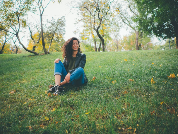 Pretty brunette long curly hair hispanic girl closeup portrait outdoors in the green park in autumn. Woman looks beautiful,smiles,laughs and flirts skittish - Foto, Imagem