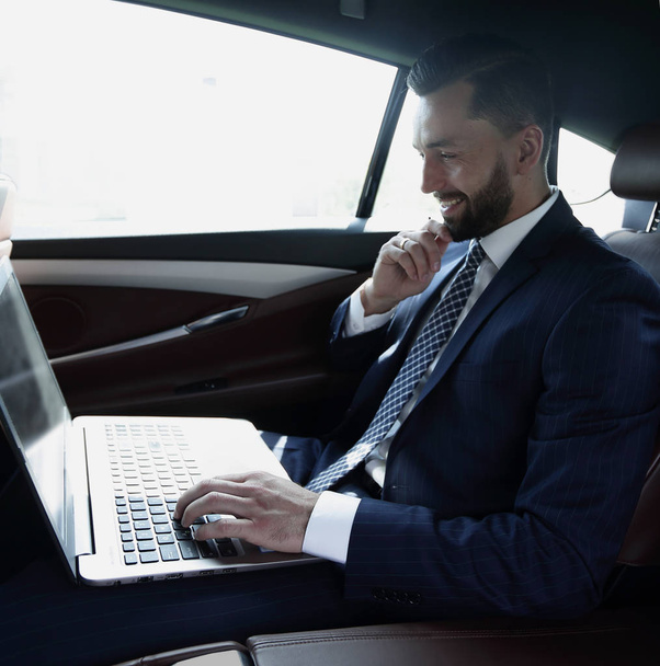 Businessman typing text on laptop while sitting in car - Foto, afbeelding