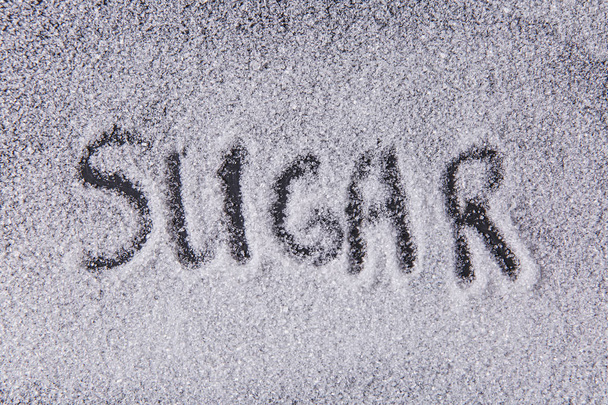 Escrito por uma palavra de dedo açúcar na textura de cristais de açúcar branco em um fundo preto
 - Foto, Imagem