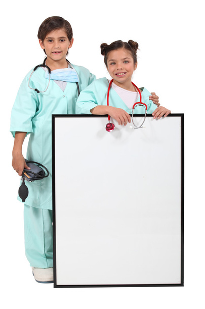 Children dressed up as doctors and standing behind a blank sign - Fotografie, Obrázek