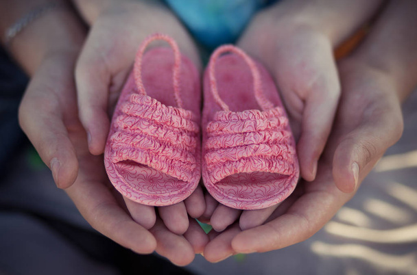 Woman and man father and mother young hands only isolated holding little baby pink shoes in emotional love heart pose.Future family happyness - Photo, Image