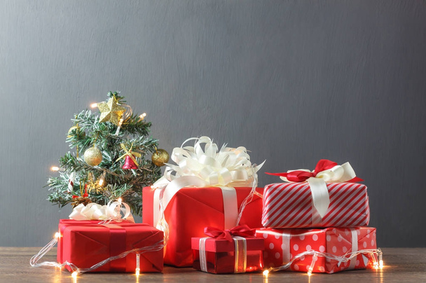 Красивые красные подарочные коробки и рождественская елка с подсветкой из современного дерева на домашнем офисном столе
. - Фото, изображение