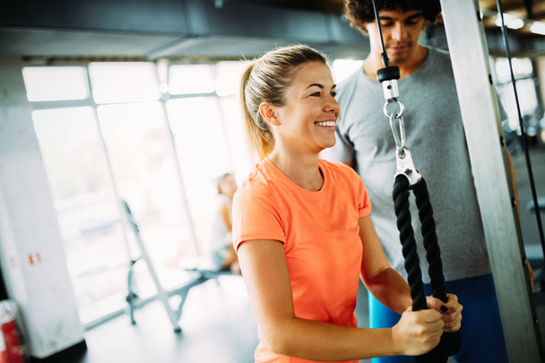 Young beautiful woman doing exercises with personal trainer in gym - Foto, Imagen