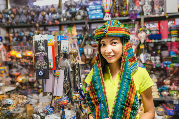 Vrouw winkelen en proberen een traditioneel Arabisch of Midden-Oosten hoofd dragen tulband in souvenir markt in Turkije - Foto, afbeelding