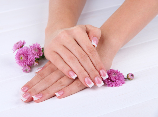 Woman hands with french manicure and flowers on white wooden background - Фото, зображення
