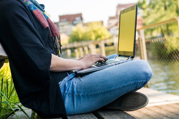 Jovem mulher usando laptop em um parque na margem do rio
. - Foto, Imagem