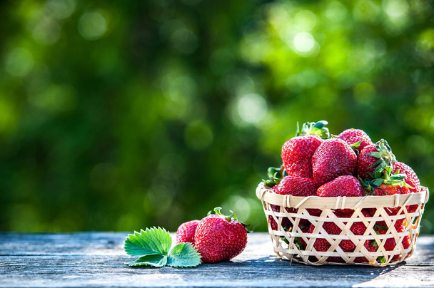 Juicy strawberries in a wicker basket, wooden table, against the - Photo, Image