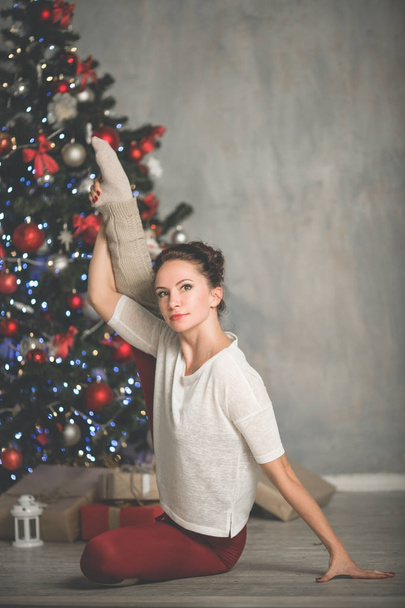 Beautiful flexible young woman is doing sports near christmas tree, sports and holiday concept - Foto, Bild
