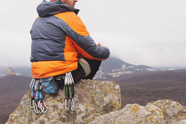 Hipster - a climber in a down jacket and a knitted cap sits and rests on the top of a rock - Photo, image