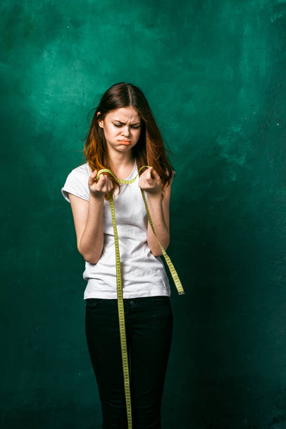 a sad girl in a white T-shirt is unhappy with her parameters, holds a measuring tape in her hands - Fotoğraf, Görsel