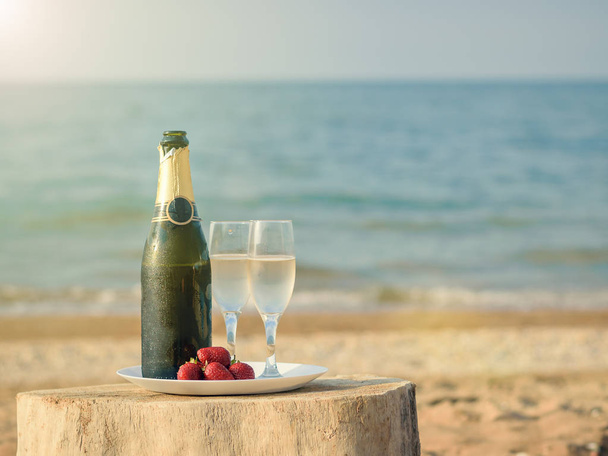 Bright rays of the sun illuminate the bottle of champagne on the beach. - Φωτογραφία, εικόνα