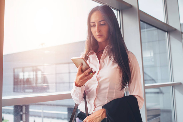 Porträt einer jungen Geschäftsfrau, die ihr Smartphone benutzt, während sie zum Boarding-Bereich des Flughafens läuft - Foto, Bild