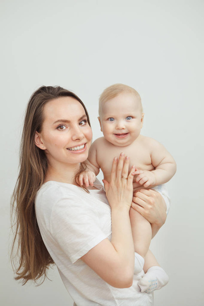 Positive mother with broad smile holds smiling baby on arms - Fotoğraf, Görsel