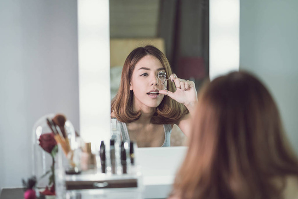 Молодая красивая азиатка делает макияж у зеркала
 - Фото, изображение