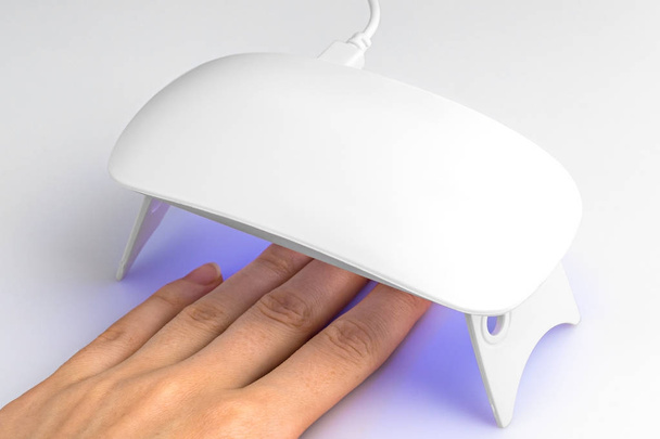 Hand in UV-lamp verlichting voor nagels op een witte achtergrond - Foto, afbeelding