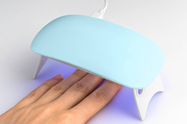 Hand in UV-lamp verlichting voor nagels op een witte achtergrond - Foto, afbeelding
