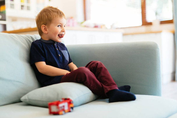 Happy boy sitting on sofa in living room - Фото, изображение