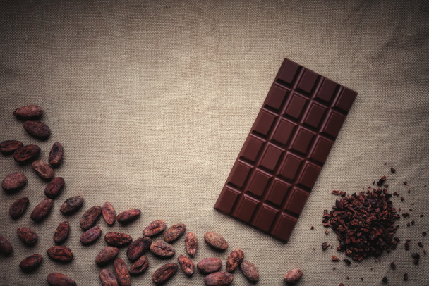 Ciemny czekolada i surowe ziarna kakaowca. Tło tekstura starych ju - Zdjęcie, obraz