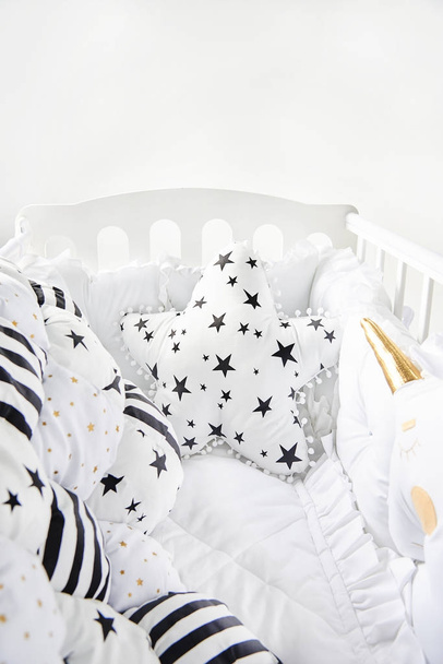 Acogedora cuna con almohadas cuadradas blancas y manta de edredón patchwork con estrellas y rayas negras
 - Foto, imagen
