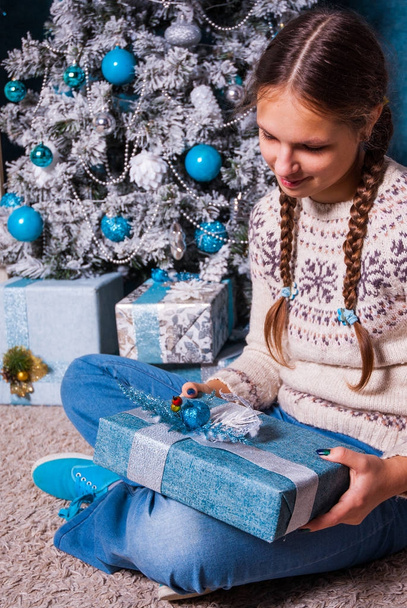 happy girl hold christmas present box on holiday morning in beautiful room interior. Female child holding Xmas gift in hands near decorated fir christmas tree and fireplace. Winter holidays concept - Foto, Imagen