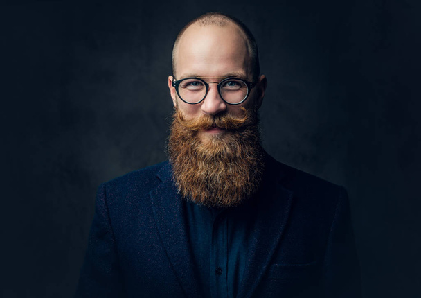 Portrait of redhead bearded male in eyeglasses dressed in an elegant wool suit over grey background. - Photo, Image