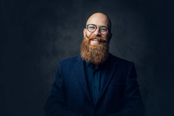 Portrait of redhead bearded male in eyeglasses dressed in an elegant wool suit over grey background. - Foto, Imagen